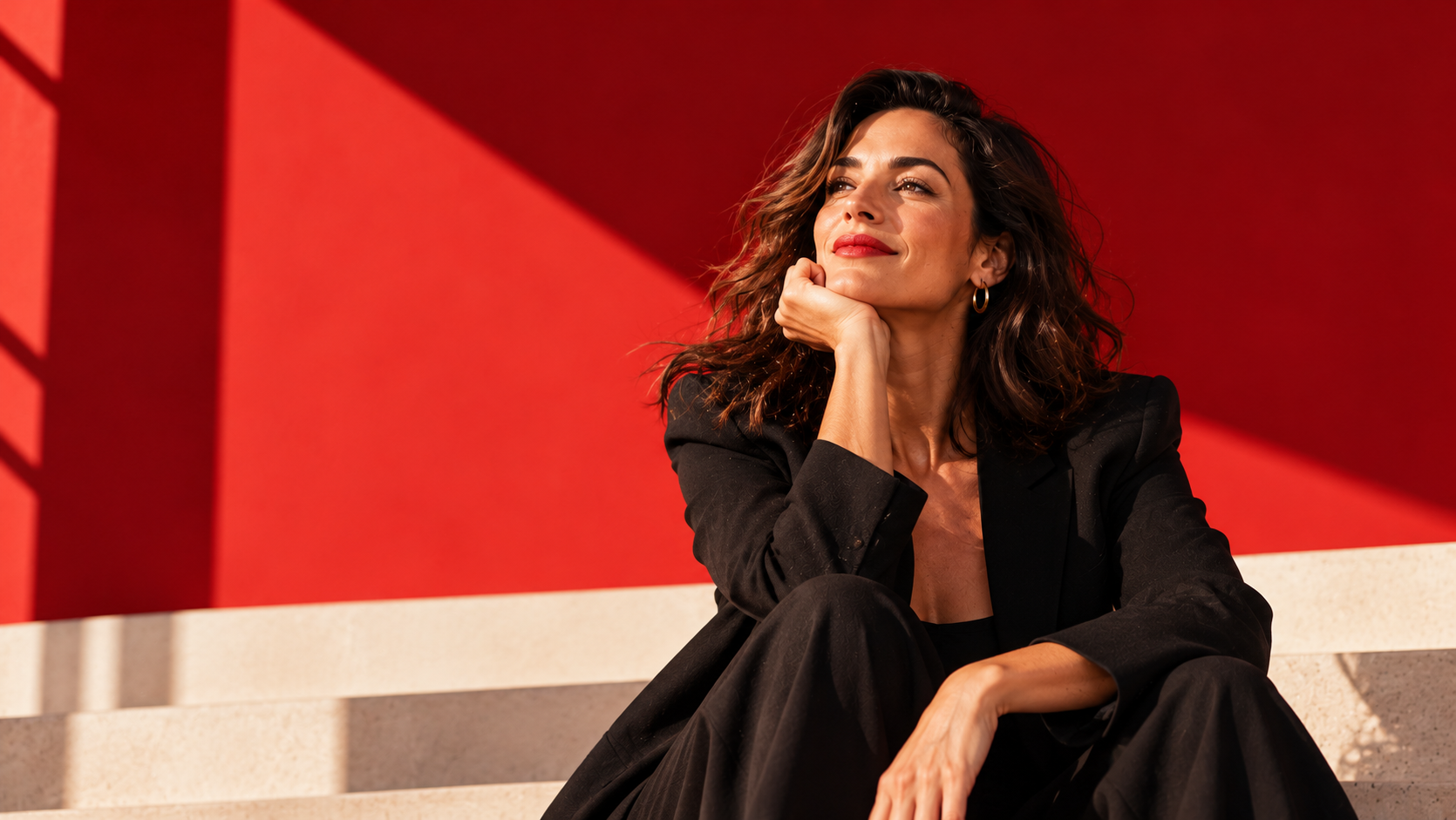 Editorial portrait of a woman in a black suit against a vibrant red architectural background