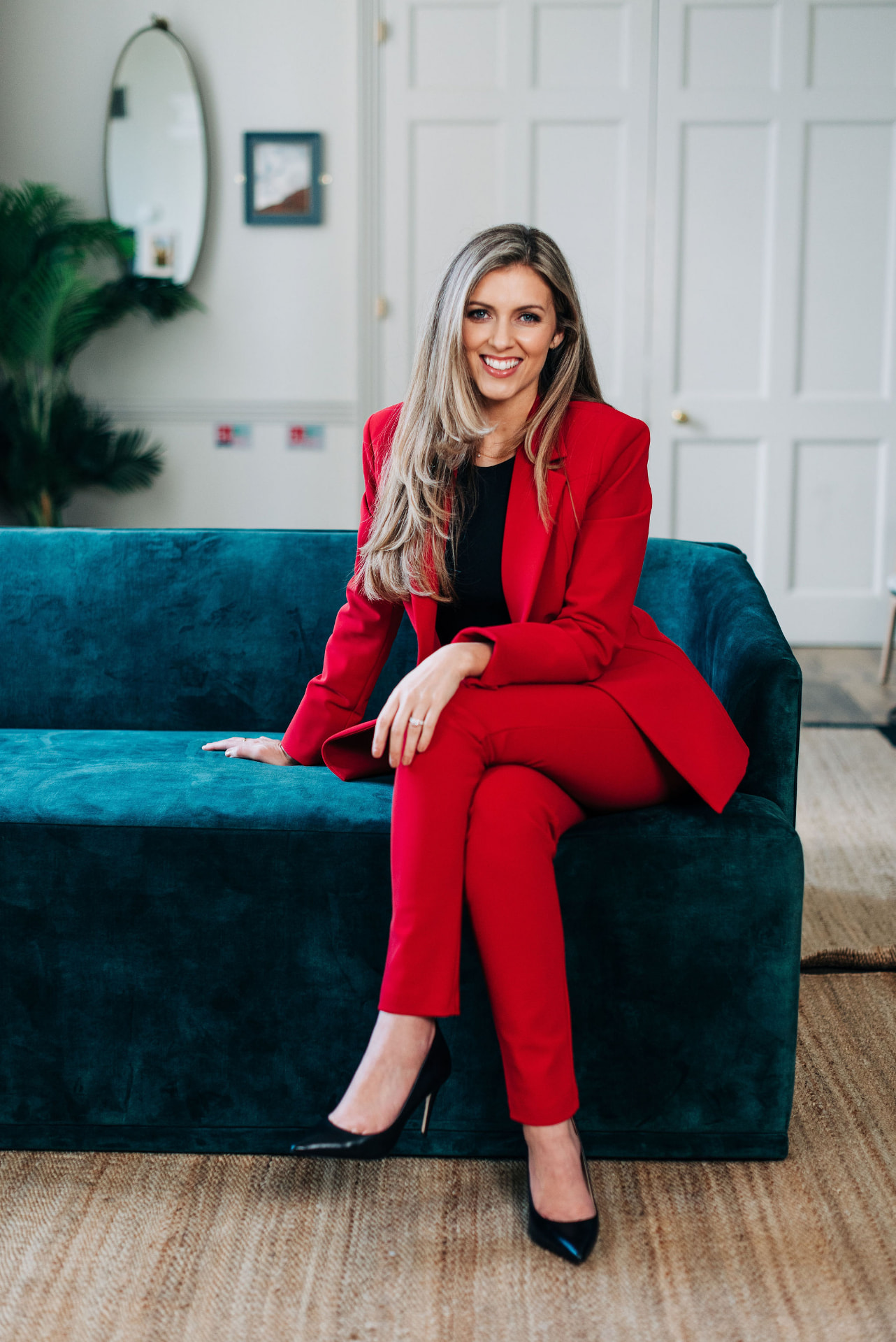 Mikaela Jackson seated on a teal sofa in a red suit