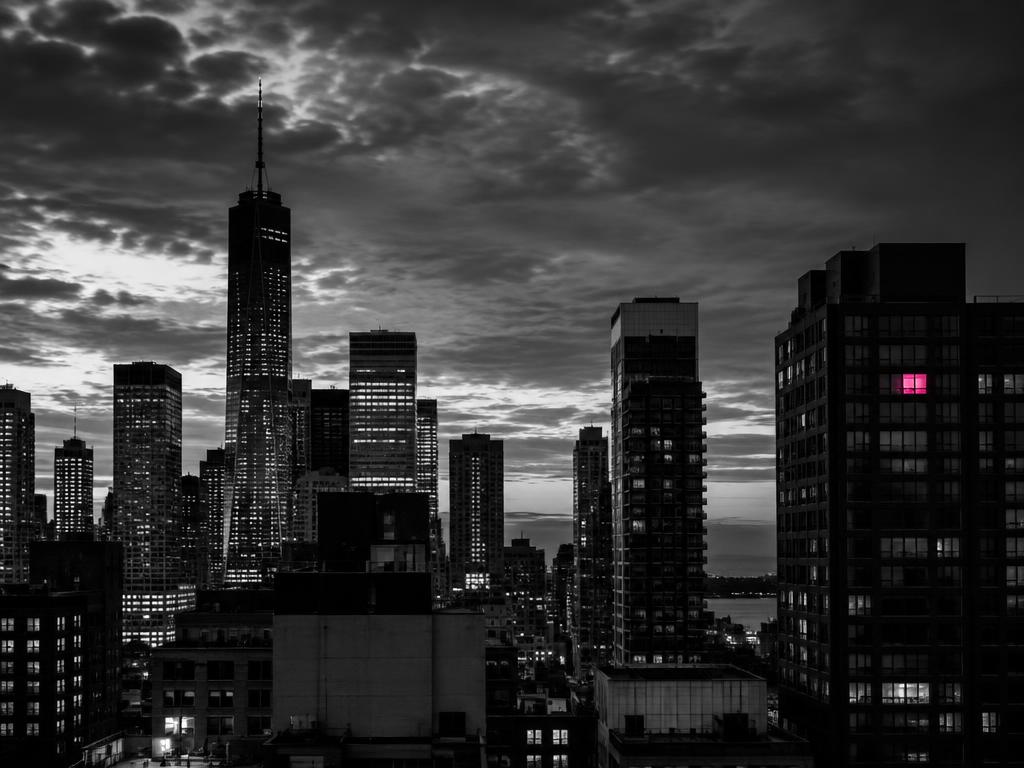 A black-and-white city skyline at dusk with a single window glowing pink in one skyscraper
